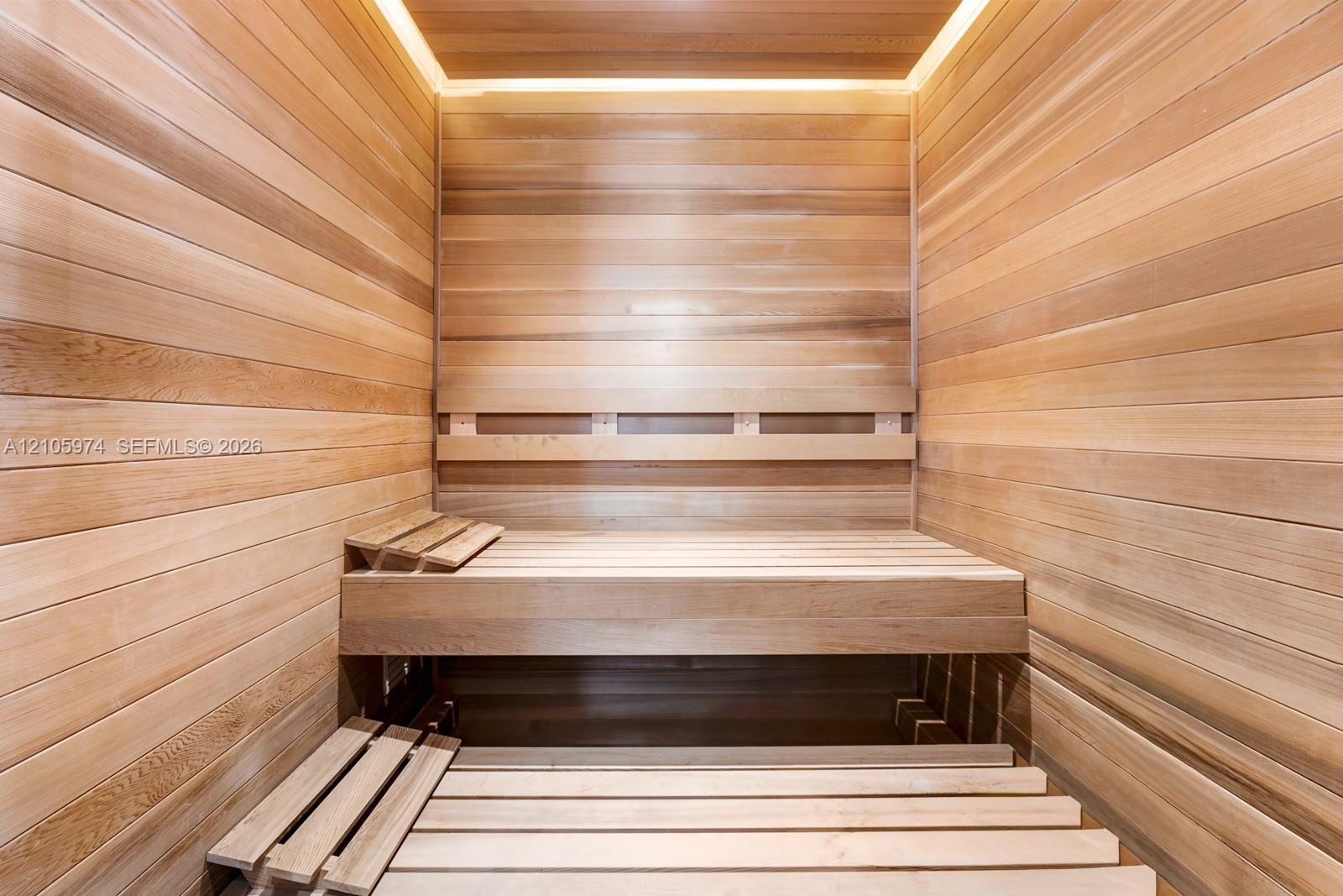 Sauna interior featuring natural wood wall paneling, tiered slatted benches, and recessed perimeter ceiling lighting