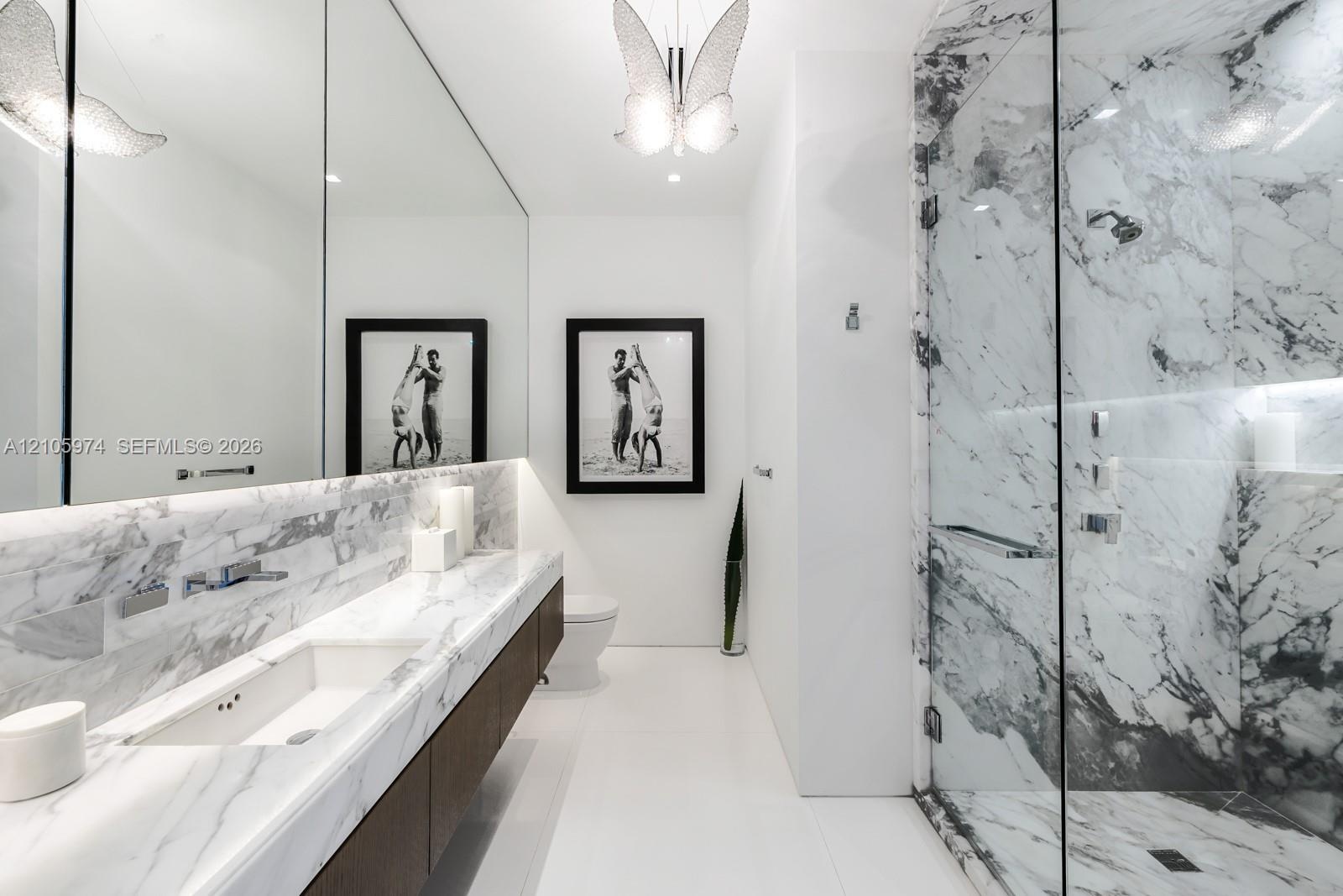Stone-surfaced vanity with an integrated basin, wall-mounted faucet, expansive wall-to-wall mirror, walk-in shower with glass enclosure, and decorativ
