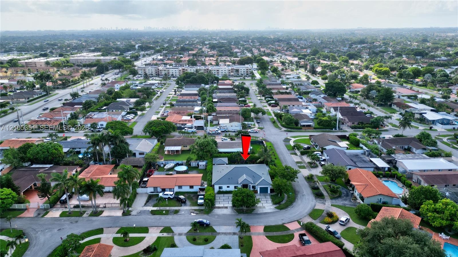 Aerial perspective of a single-story residence featuring a multi-pitched hip roof, a concrete-paved driveway, and a fenced perimeter