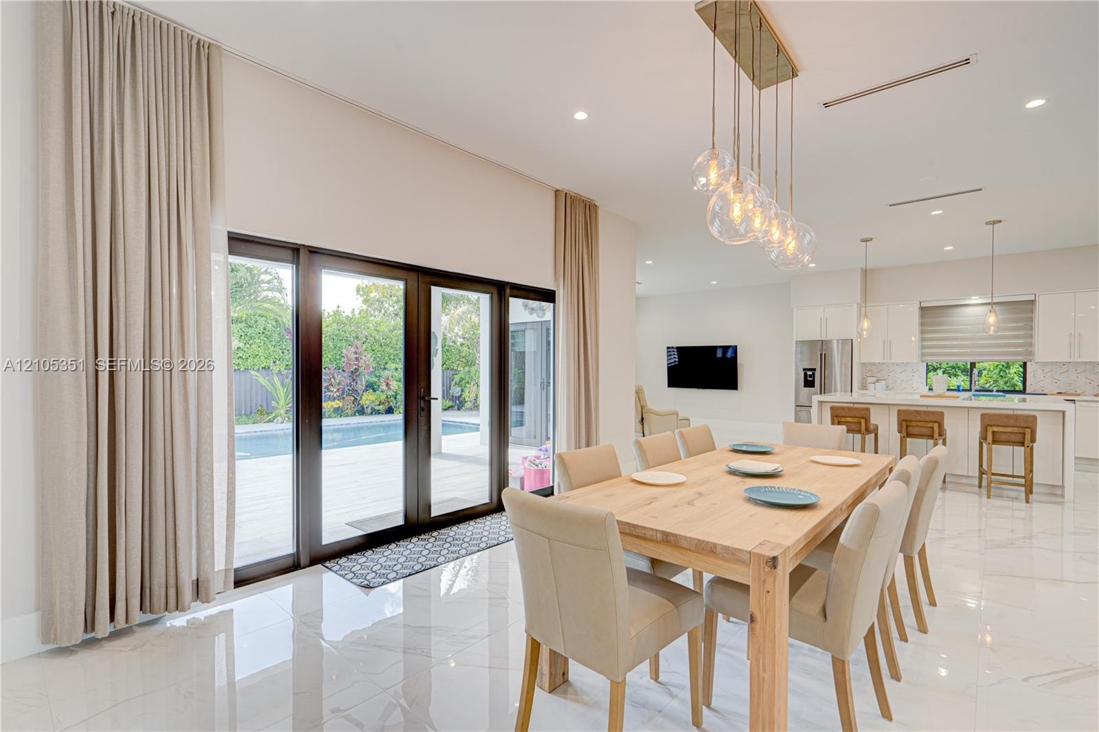 Open-concept interior featuring large-format polished tile flooring, floor-to-ceiling glass panel doors, a multi-light contemporary glass chandelier, 