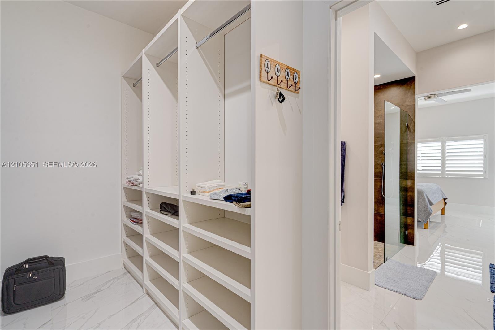 Walk-in closet featuring floor-to-ceiling custom white built-in shelving, hanging rods, and stone-finish tile flooring