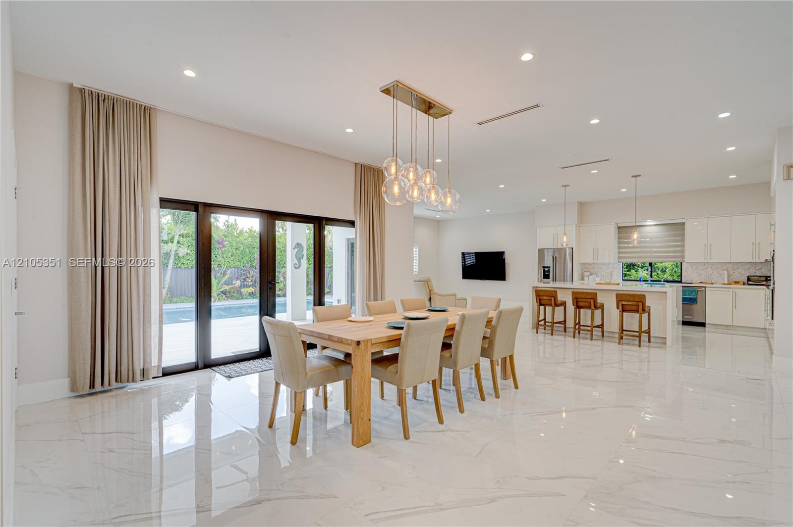 Open-concept interior featuring large-format polished stone flooring, recessed lighting, a modern multi-pendant chandelier, white slab-front cabinetry