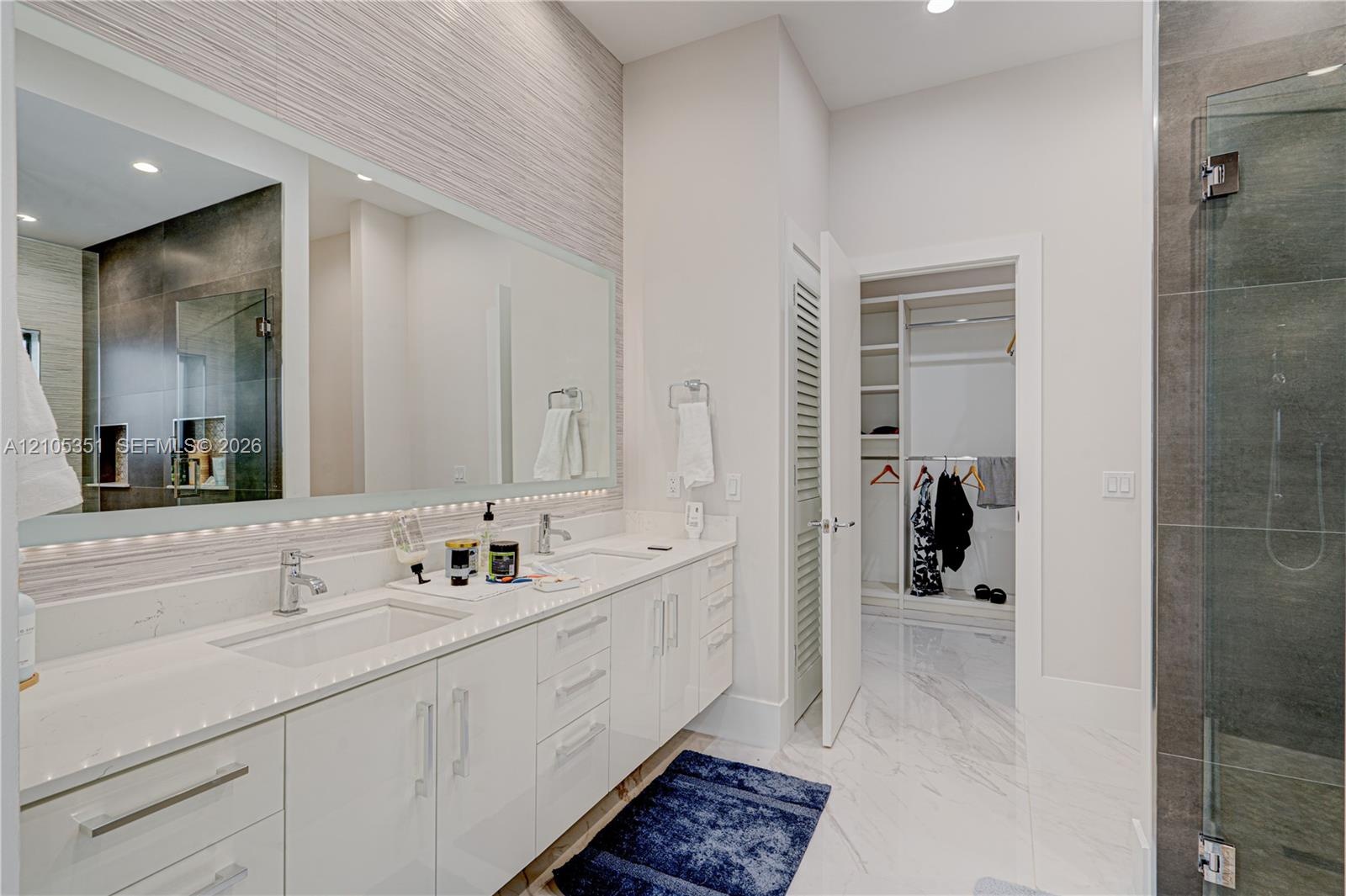 Double vanity featuring white cabinetry, quartz countertops, integrated under-mount sinks, and an expansive wall-to-wall mirror with under-cabinet lig