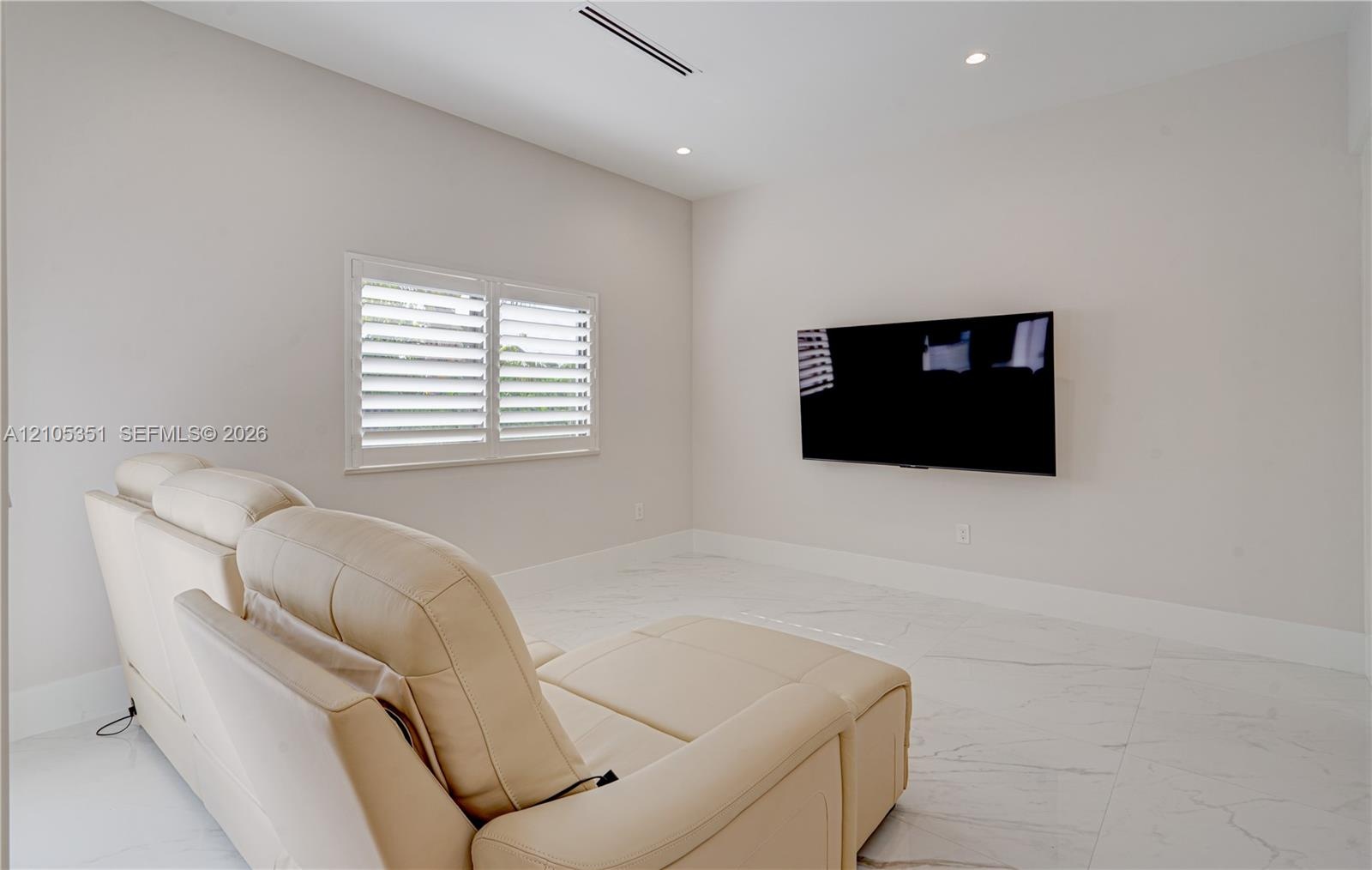 Neutral-toned interior featuring large-format tile flooring, recessed ceiling lighting, a wall-mounted linear HVAC vent, and a window fitted with whit