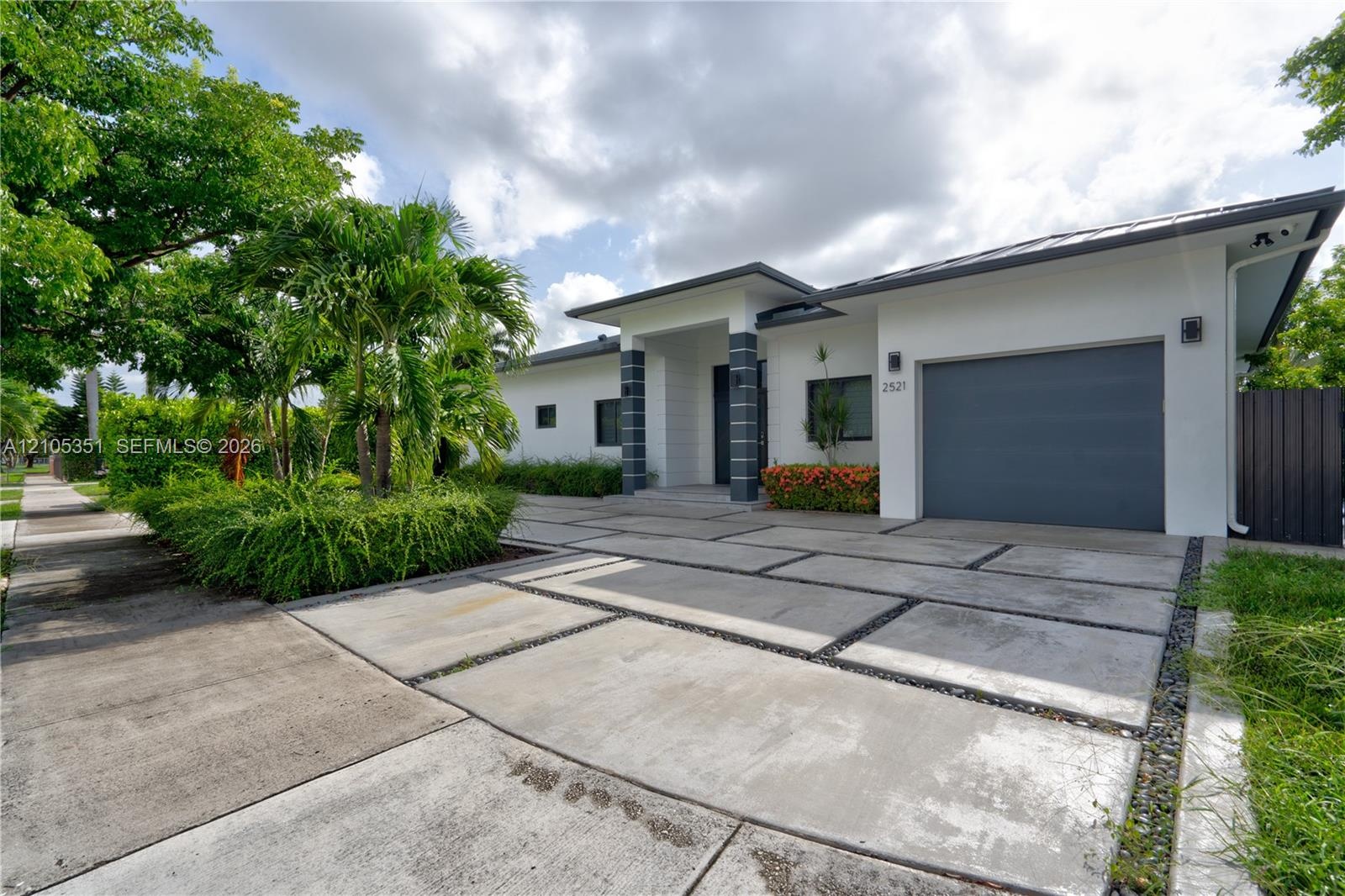 Contemporary single-story exterior featuring white stucco siding, a charcoal-toned garage door, geometric concrete paver driveway with decorative ston