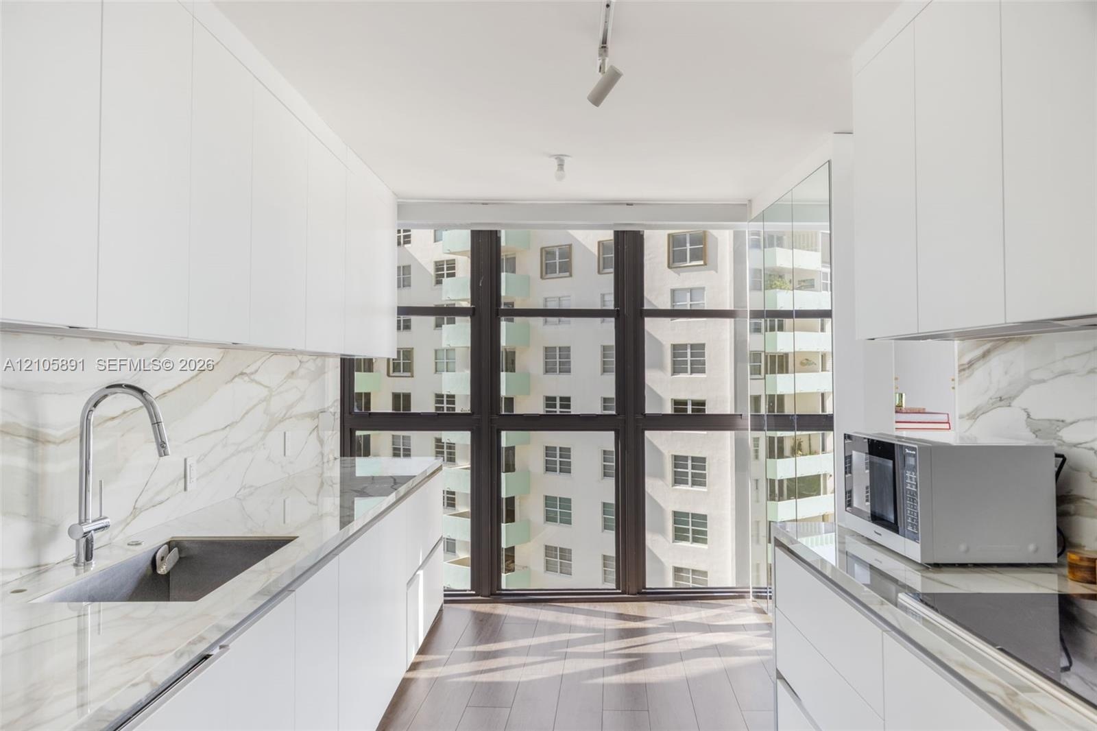 Kitchen featuring white flat-panel cabinetry, floor-to-ceiling windows, veined stone-finish countertops and backsplash, wood-finish flooring, and a st