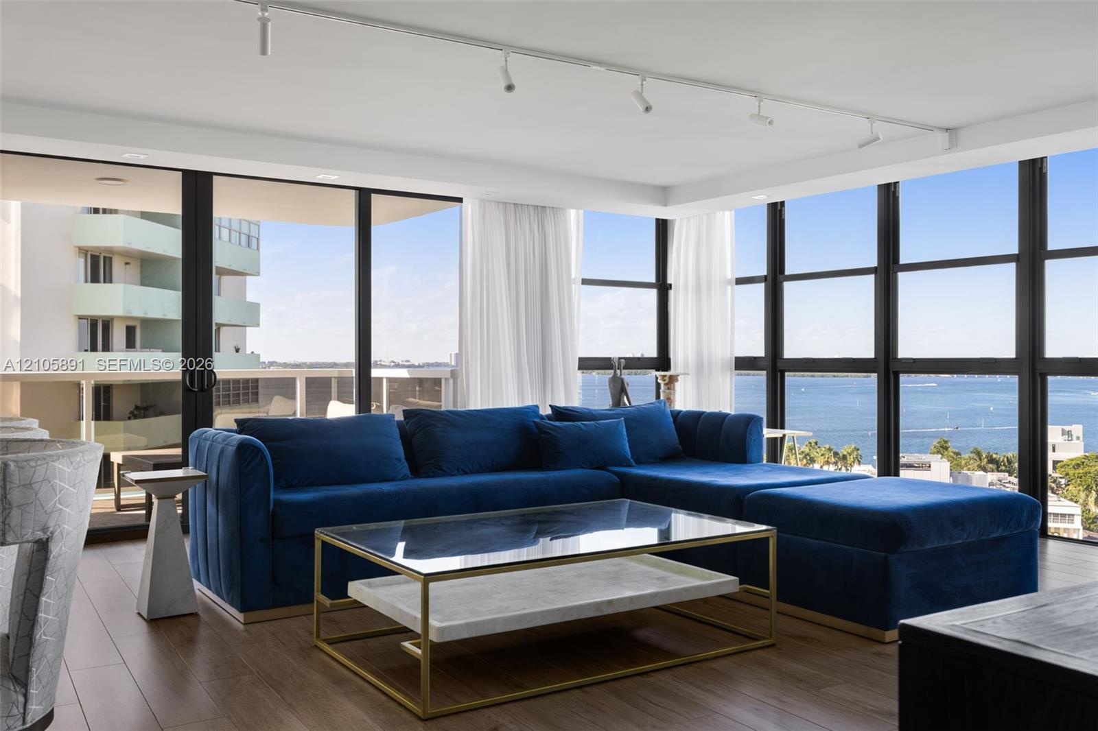 Floor-to-ceiling windows with black metal frames, wood-finish flooring, ceiling-mounted track lighting, and a sliding glass door opening to a private 