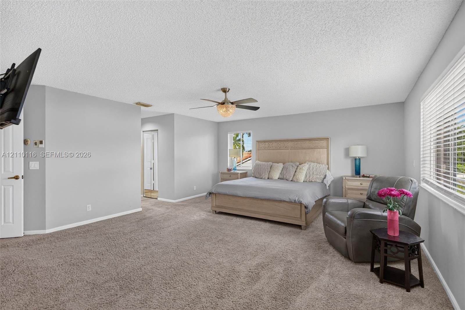 Spacious room featuring neutral carpeting, a central ceiling fan with integrated lighting, and horizontal blinds on the windows