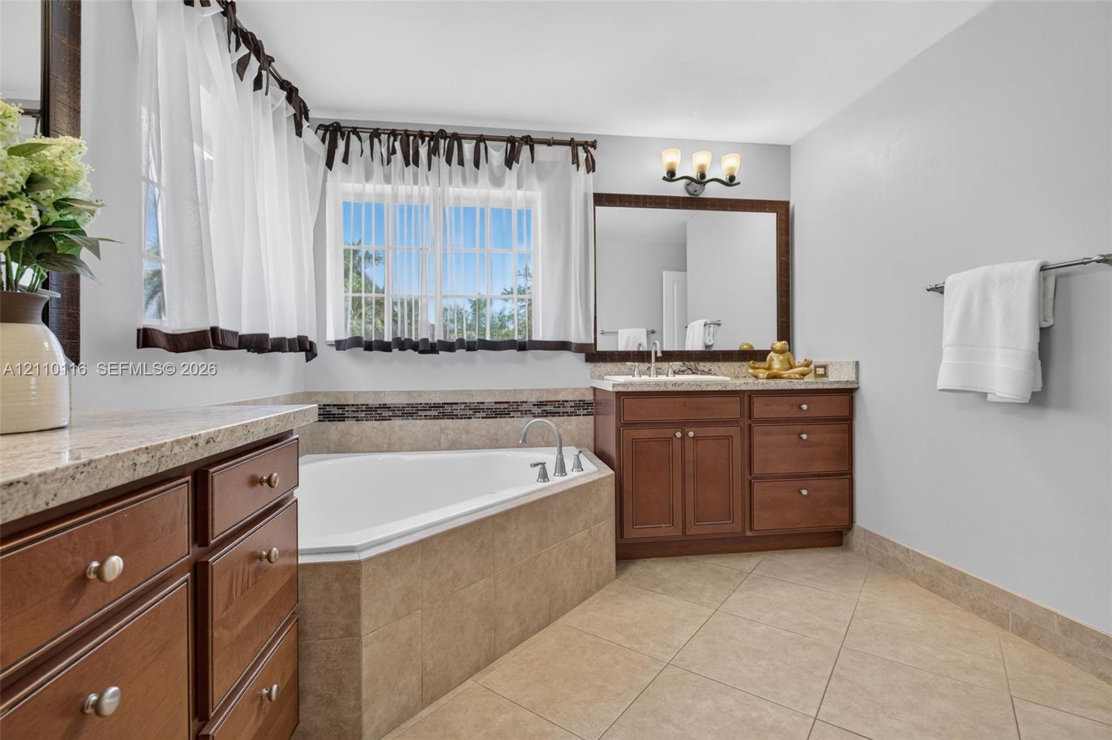 Bathroom featuring a corner soaking tub with tile surround, wood cabinetry, stone-finish countertops, ceramic tile flooring, and a large framed vanity