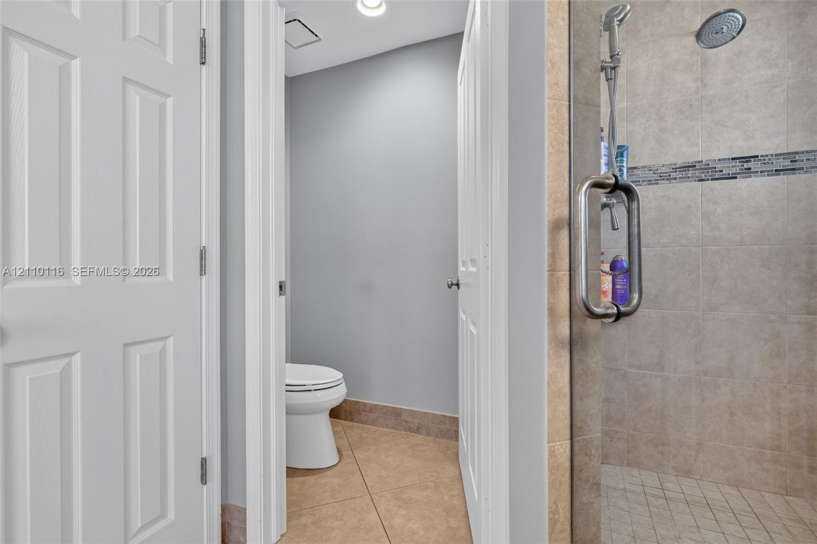 Walk-in shower with a glass door, rainfall showerhead, and tile surround featuring a decorative mosaic accent band, accompanied by tile flooring and w