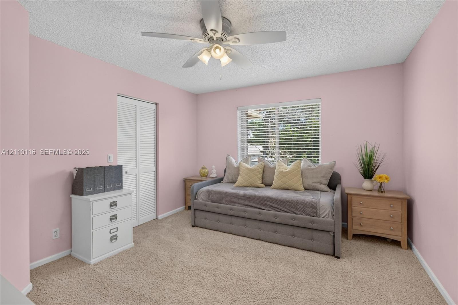 Neutral-toned carpeting, ceiling fan with integrated light fixture, window with horizontal blinds, and closet with white louvered doors