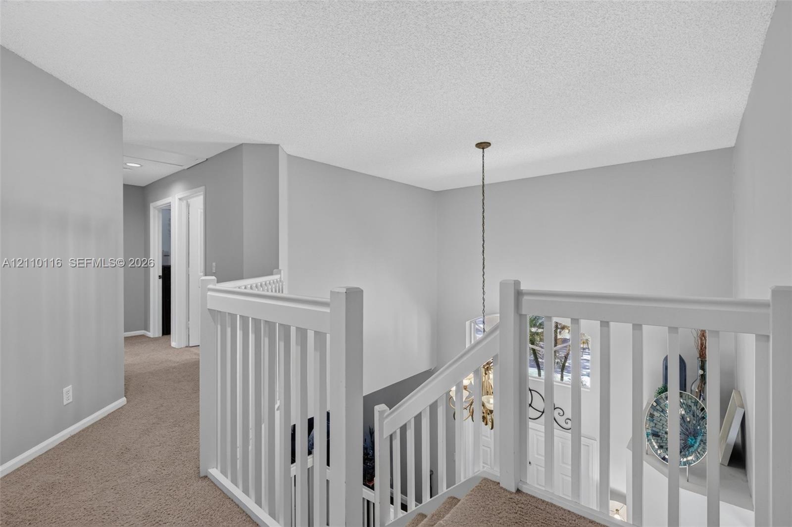 Landing area featuring neutral carpeting, white wooden balustrade, and a multi-light hanging chandelier