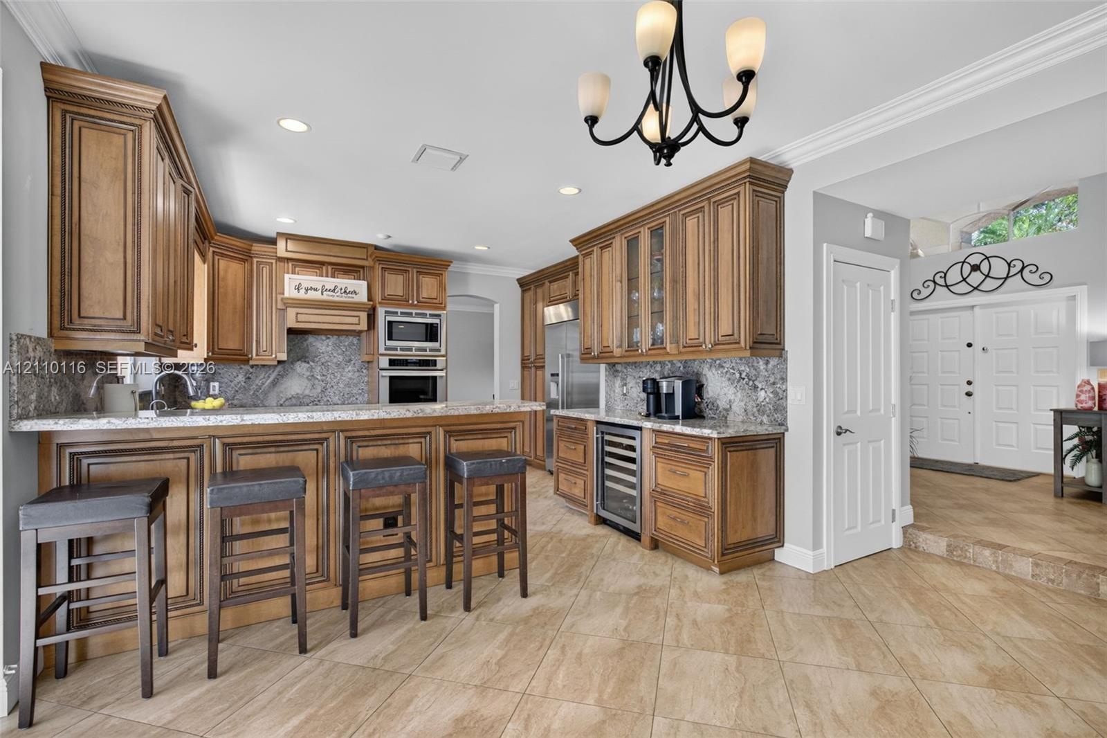 Kitchen featuring custom raised-panel wood cabinetry, stone countertops, integrated beverage refrigerator, recessed lighting, and a multi-arm chandeli