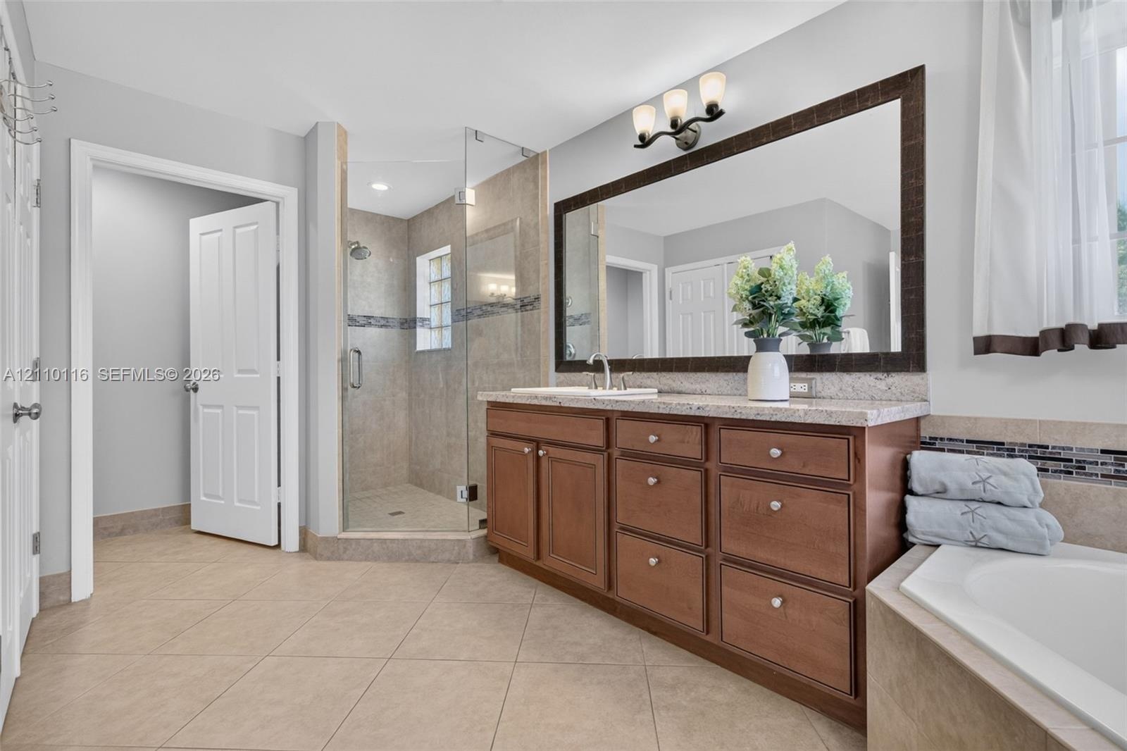 Bathroom featuring a natural wood-finish vanity with stone-surfaced countertop, glass-enclosed shower with tile surround, large framed wall mirror, an