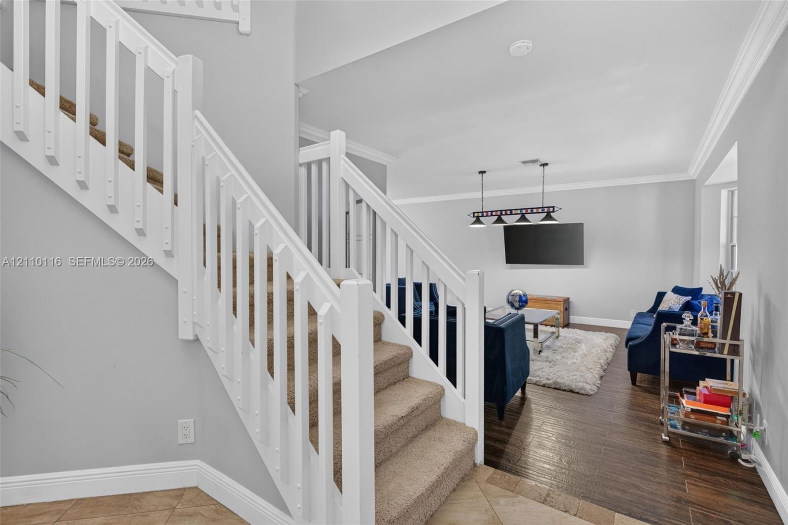 Staircase featuring white balusters and handrail, neutral-tone carpeting, wood-finish flooring, and crown molding