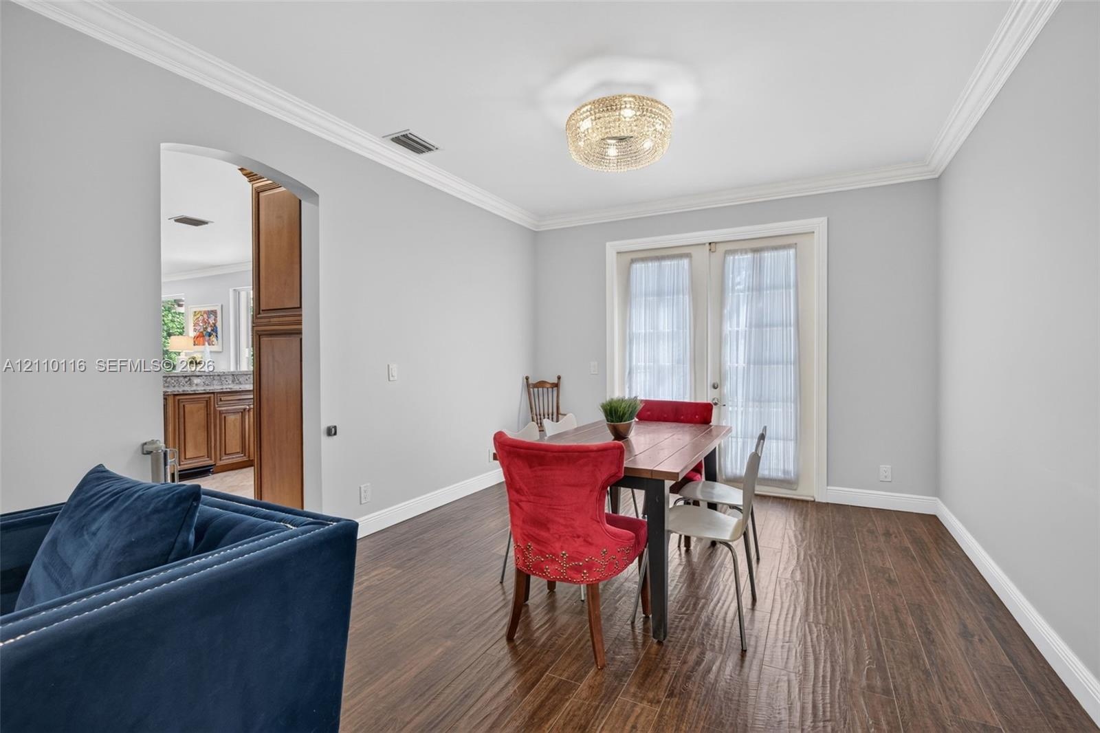 Wood-finish flooring, crown molding, a decorative circular flush-mount light fixture, and French doors