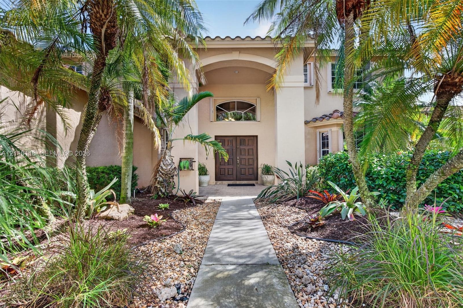 Stucco exterior featuring an arched entryway, double wood doors, arched transom window, and a tile roof