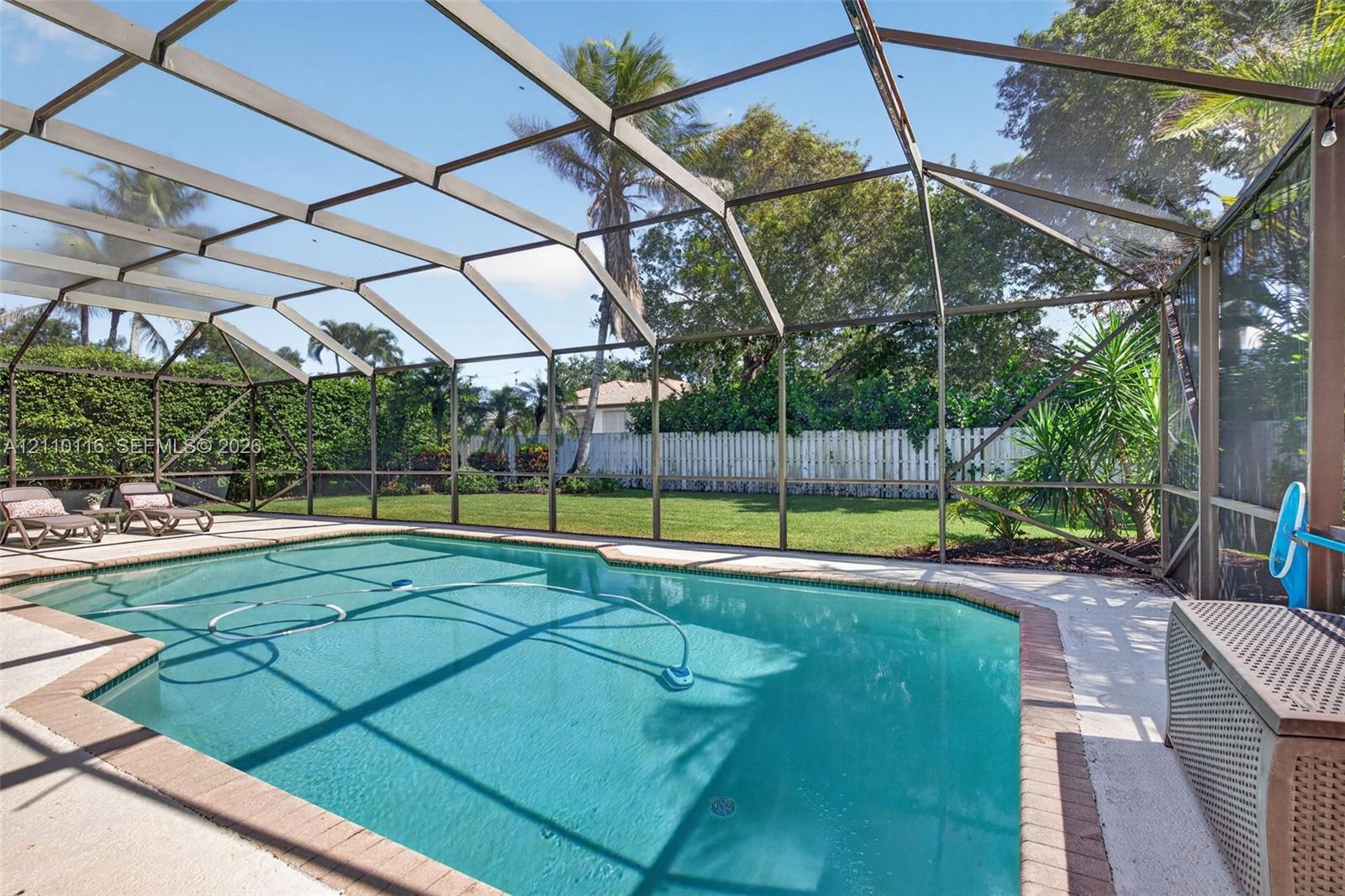 Screened-in pool area featuring a paved deck, manicured lawn, and perimeter privacy fencing