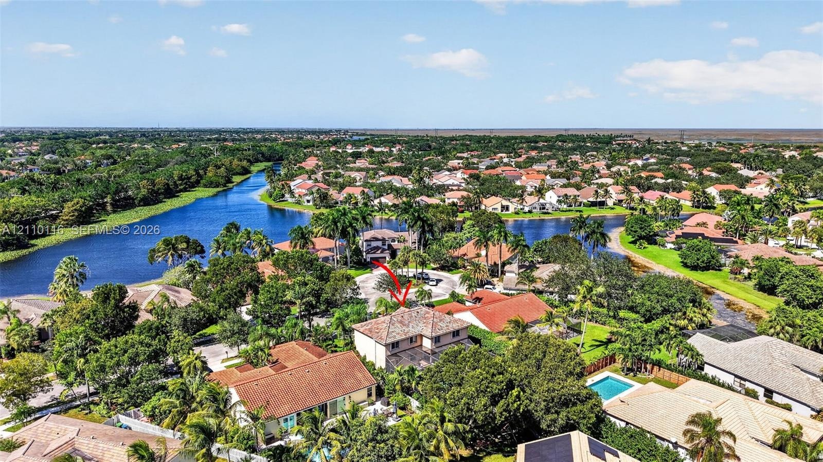 Aerial perspective of property featuring a multi-story residence with a tile roof, situated in a community with expansive water frontage and mature la