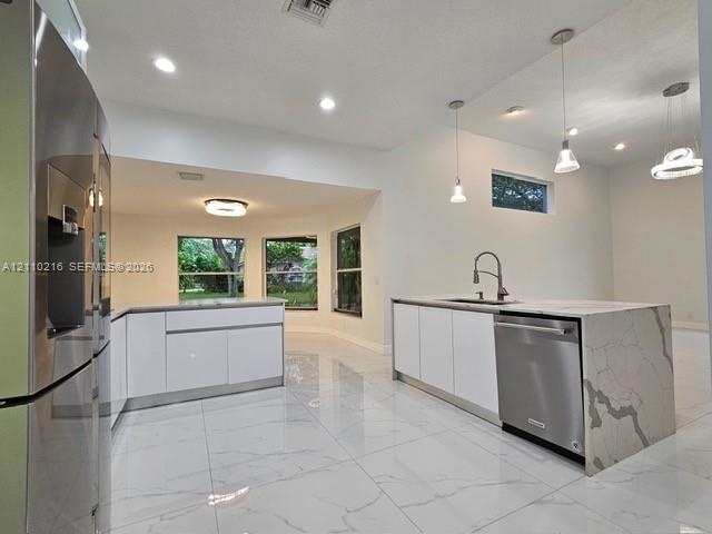 Kitchen featuring high-gloss white cabinetry, large-format tile flooring, a stone-surface island with waterfall edge, stainless steel appliances, and 