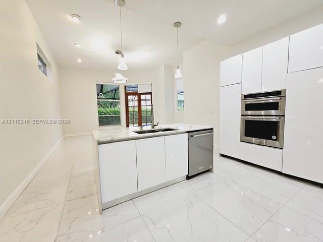 Modern kitchen featuring floor-to-ceiling white cabinetry, stone-finish countertops, stainless steel double wall ovens, a central island with an integ