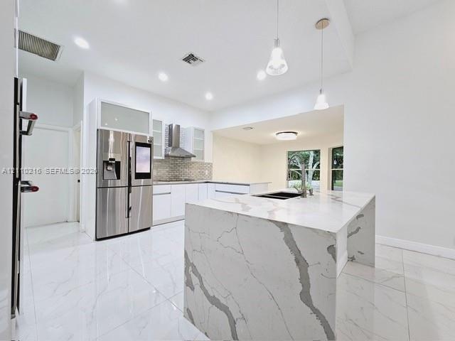 Kitchen featuring a waterfall-edge island with stone-finish countertops, stainless steel appliances, white cabinetry with glass-panel uppers, tile bac