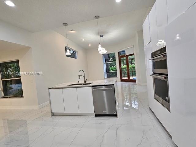 Modern kitchen featuring high-gloss white cabinetry, a center island with a stone-finish countertop, stainless steel double wall ovens, a stainless st