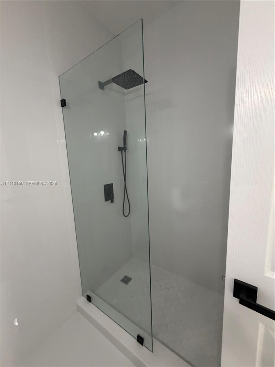 Walk-in shower featuring a frameless glass panel, matte black wall-mounted fixtures, a square rain-style showerhead, and a hand-held sprayer
