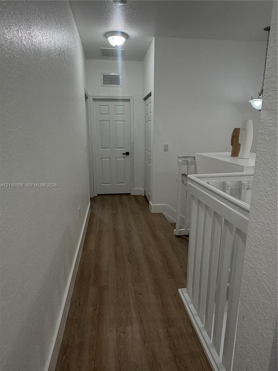 Hallway featuring wood-finish flooring, white six-panel interior doors, and a painted wooden railing