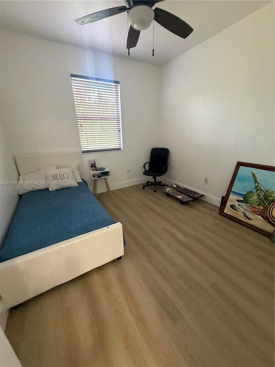 Room featuring wood-finish flooring, a neutral color palette, and a ceiling-mounted fan with integrated light fixture