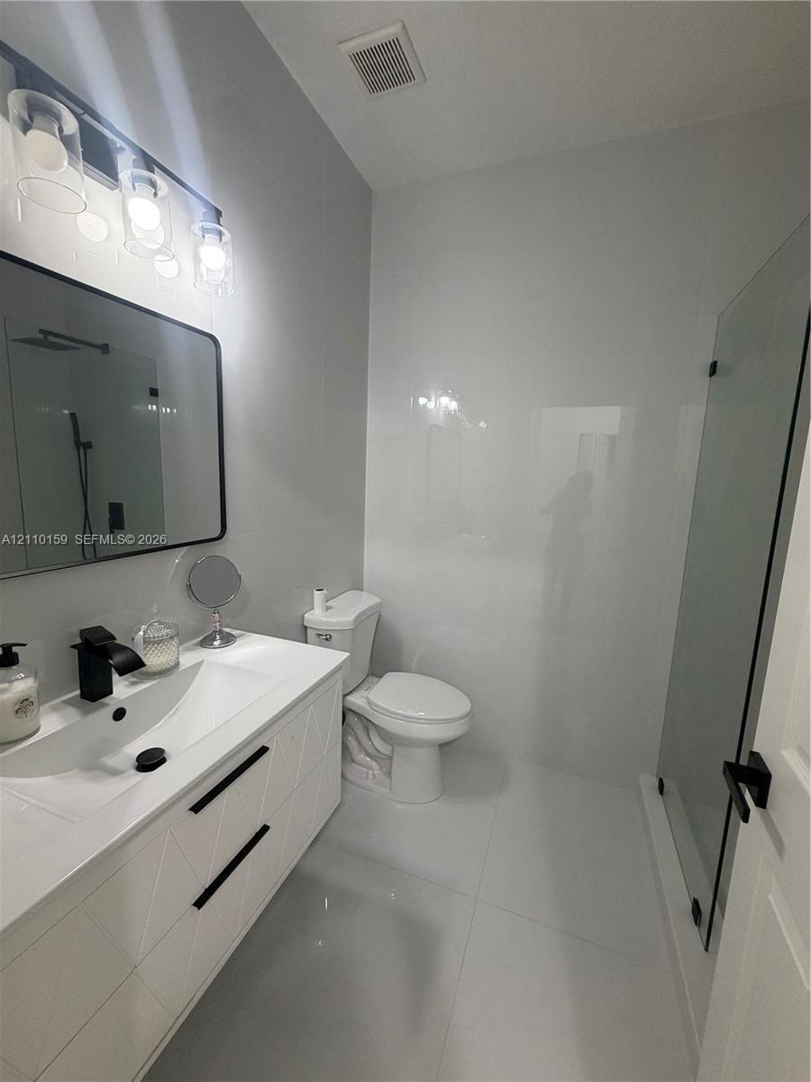 Bathroom featuring a white geometric-pattern vanity, rectangular vessel sink, matte black faucet, wall-mounted rectangular mirror, and glass-enclosed 