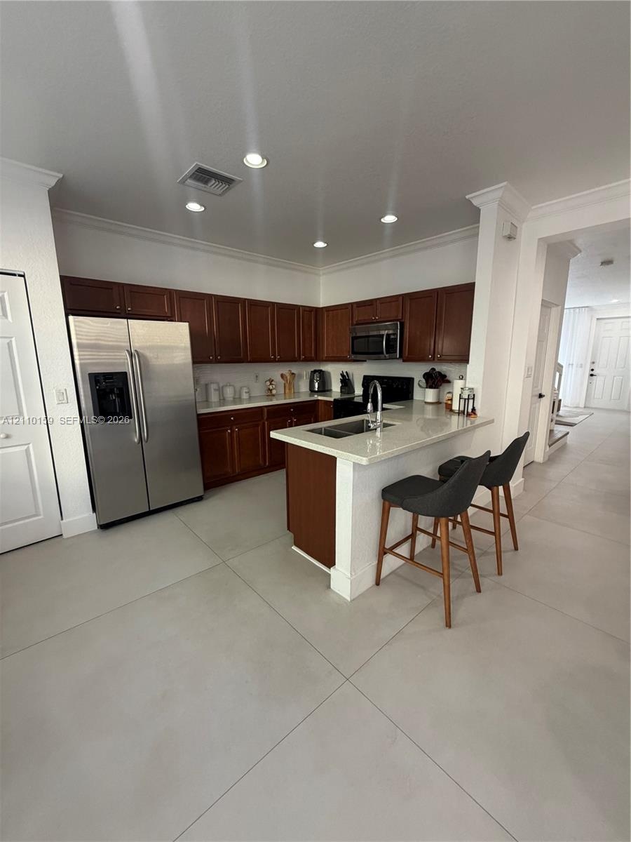 Kitchen featuring dark-toned cabinetry, light-colored countertops, stainless steel appliances, a peninsula with an undermount sink, and recessed light
