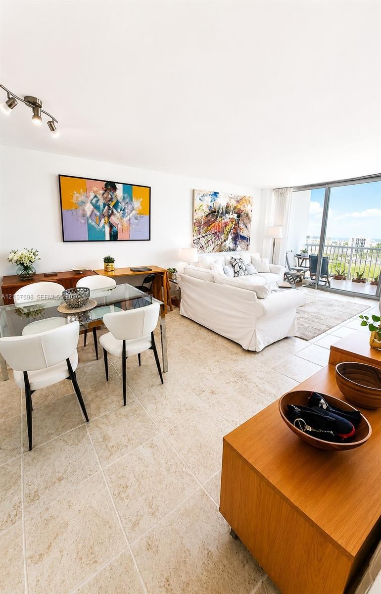 Open-concept room featuring light-toned tile flooring, adjustable multi-head track lighting, floor-to-ceiling glass sliding doors, and a private balco