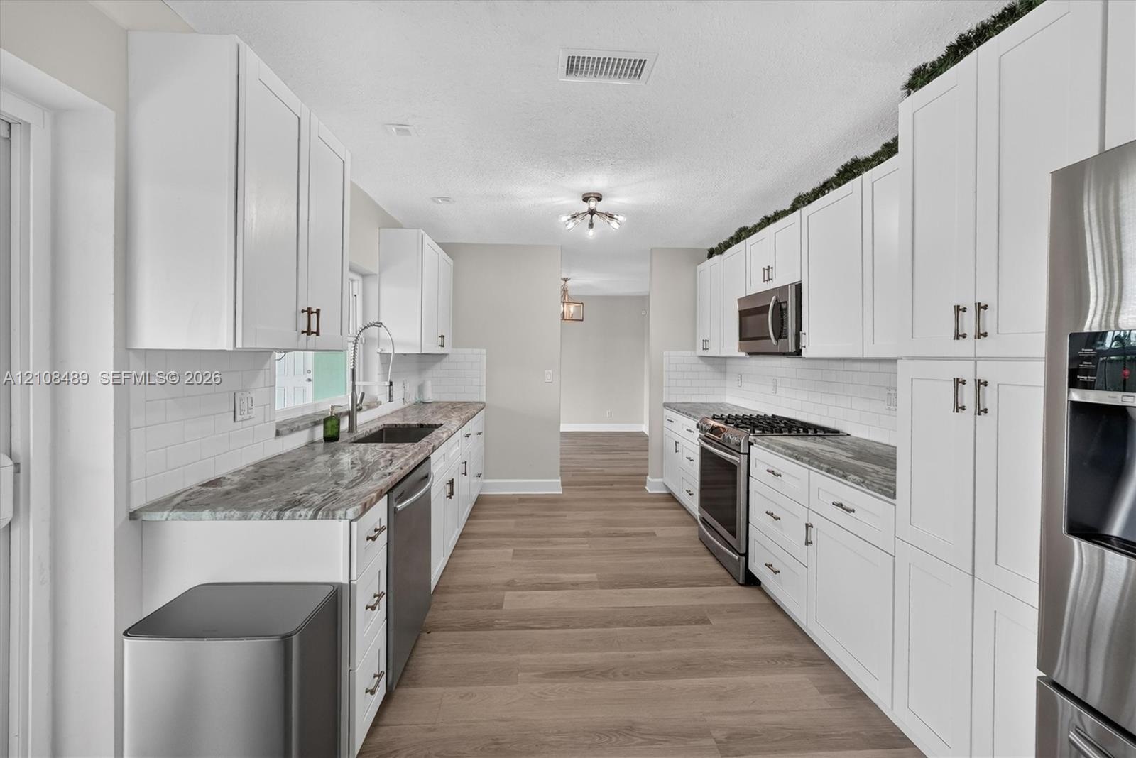 Kitchen featuring white shaker-style cabinetry, stone-patterned countertops, white subway tile backsplash, stainless steel appliances, and wood-finish
