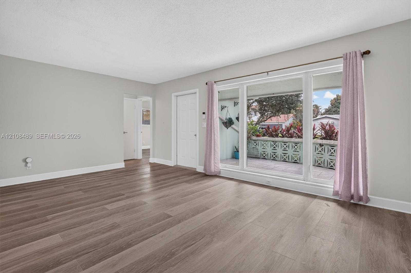Living area featuring wood-finish flooring, neutral wall paint, and a large multi-pane window with a decorative concrete screen wall exterior