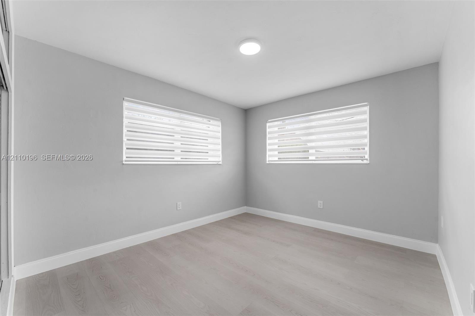Neutral-toned interior featuring wood-finish flooring, light grey walls, recessed ceiling lighting, and windows equipped with dual-layered roller shad