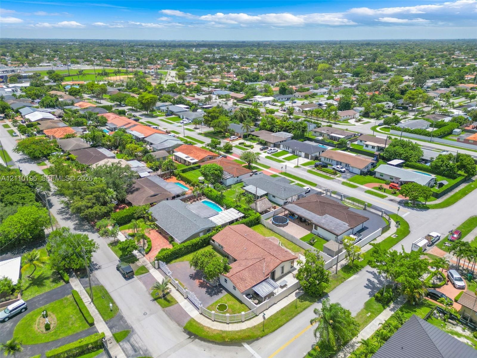 Aerial perspective of a corner lot property featuring a clay tile roof, concrete paved driveway, perimeter wall, and manicured landscaping