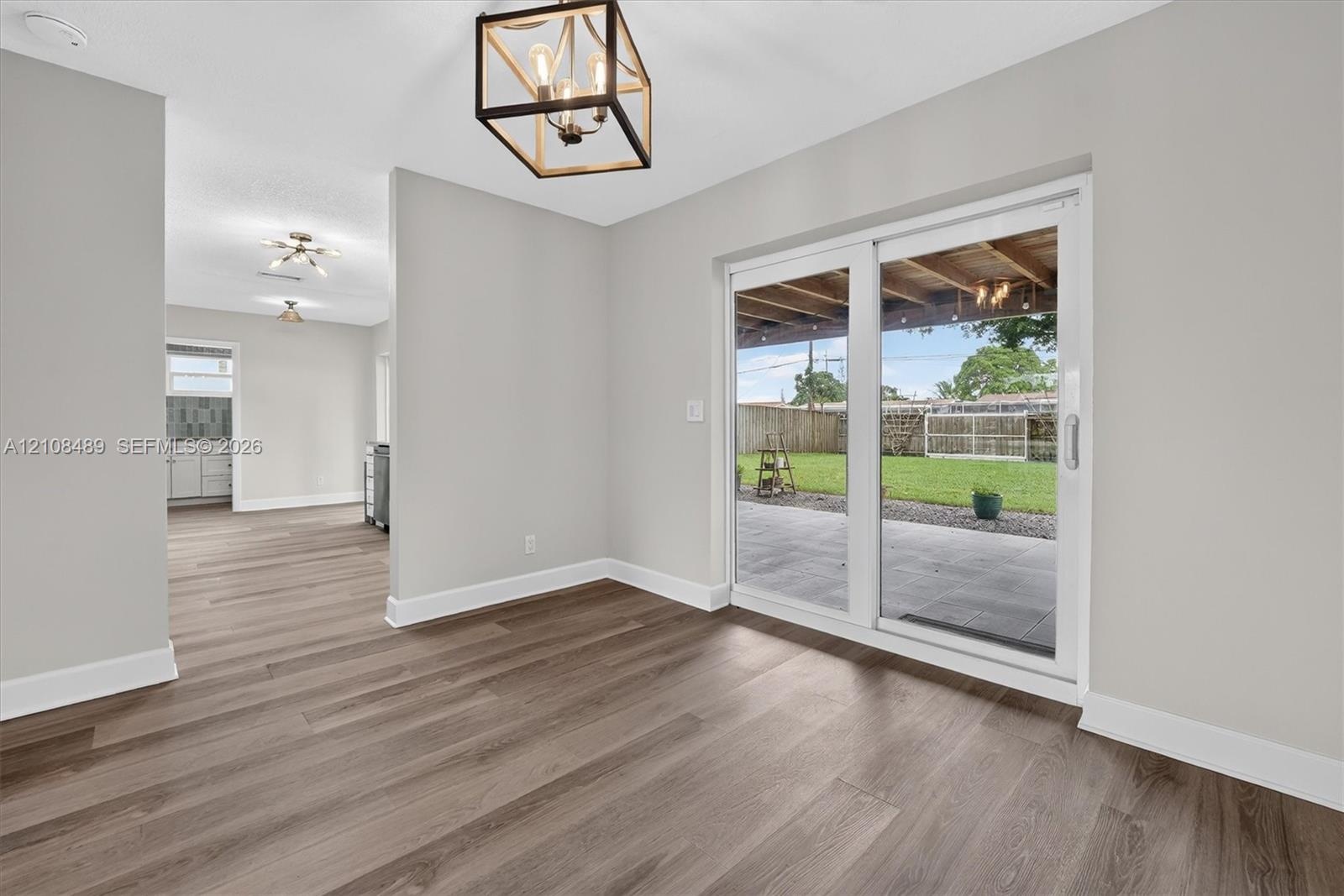 Wood-finish flooring, metal geometric chandelier, and sliding glass doors opening to a covered patio and fenced yard