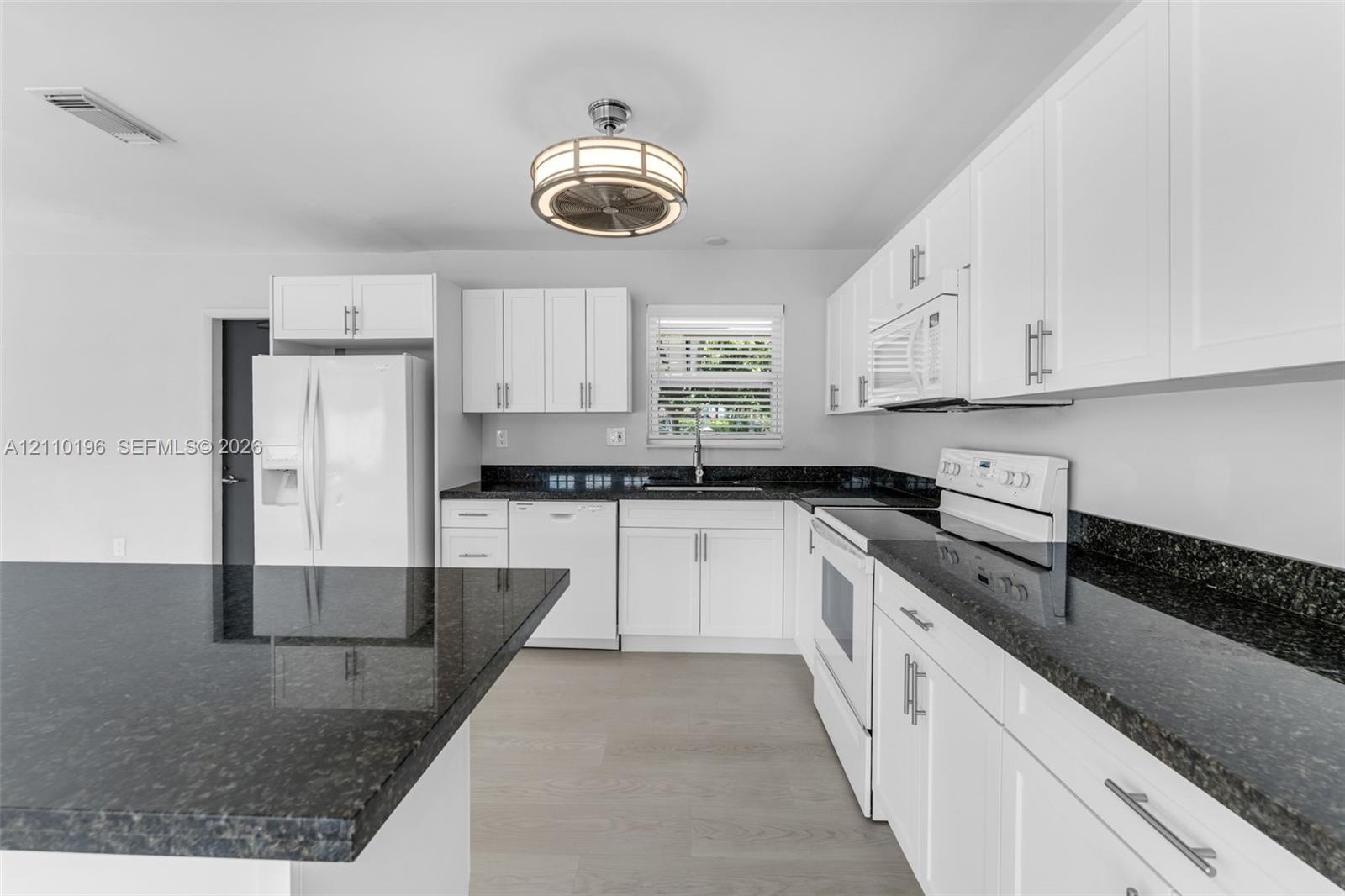 Kitchen featuring white shaker-style cabinetry, dark stone countertops, an integrated island, wood-finish flooring, and a drum-style ceiling light fix