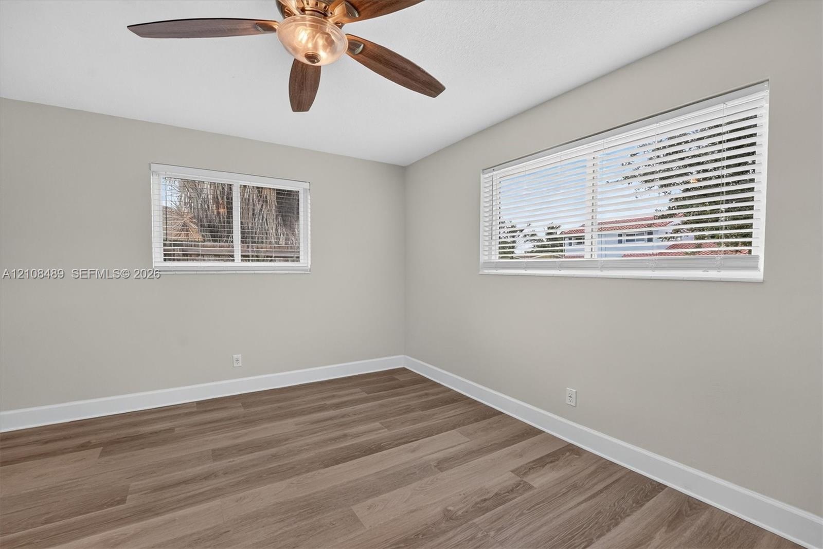 Interior space featuring wood-finish flooring, two dual-pane windows with horizontal blinds, and a multi-blade ceiling fan with integrated light fixtu