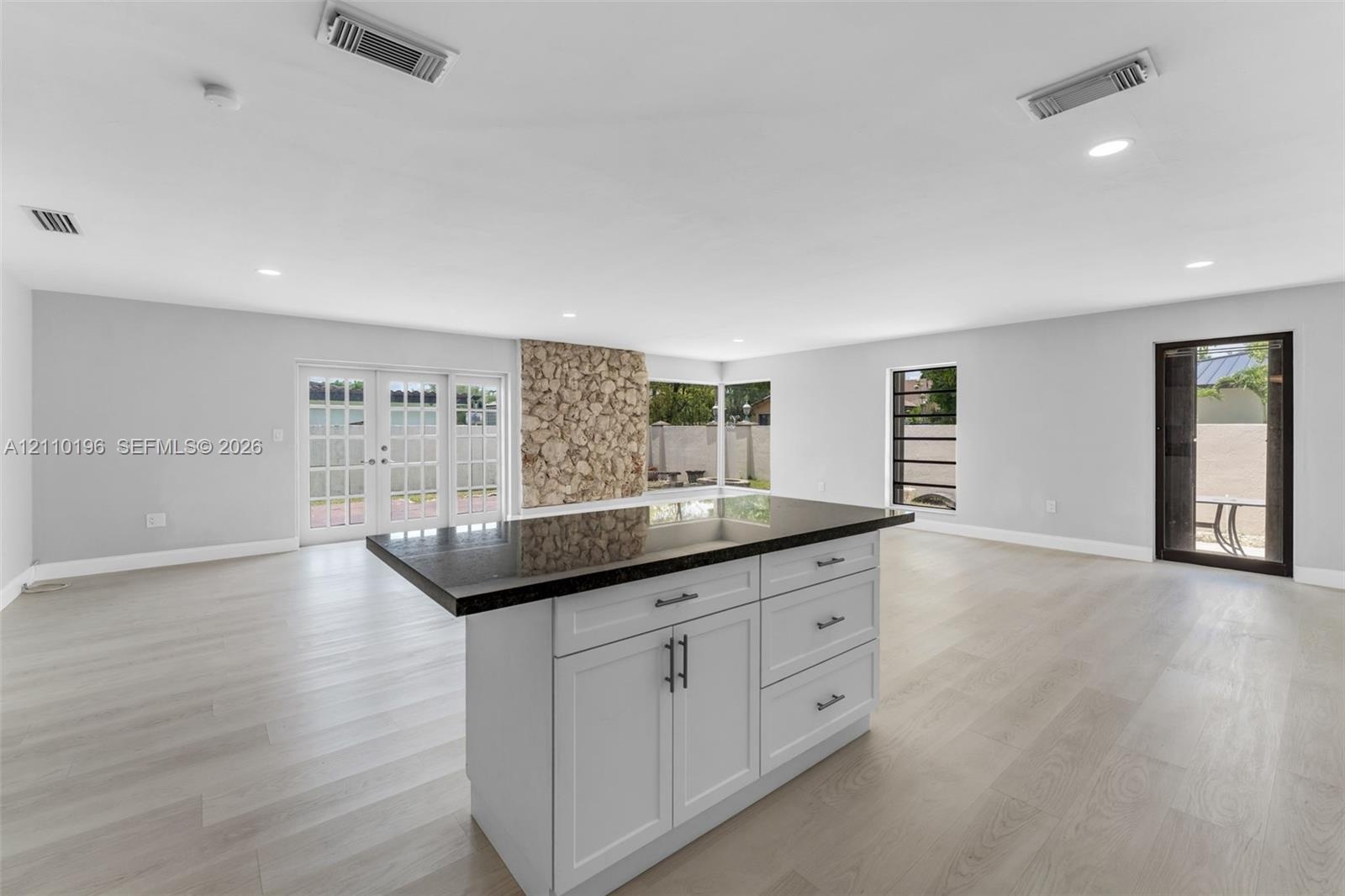 Center island featuring shaker-style cabinetry, dark stone countertop, and recessed lighting, accented by a floor-to-ceiling natural stone feature wal