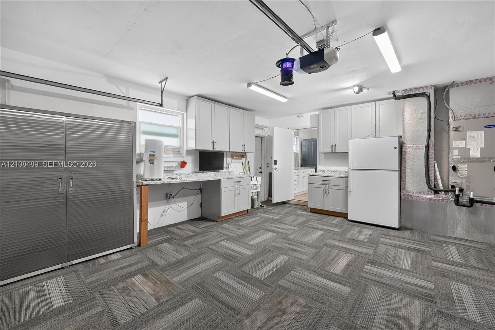 Garage featuring modular carpet tile flooring, built-in light-grey cabinetry, light-colored countertops, and integrated linear lighting