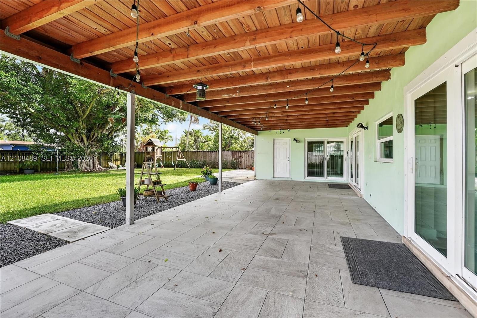 Covered patio featuring large-format stone-style tile flooring, exposed wood-beam ceiling, and sliding glass doors