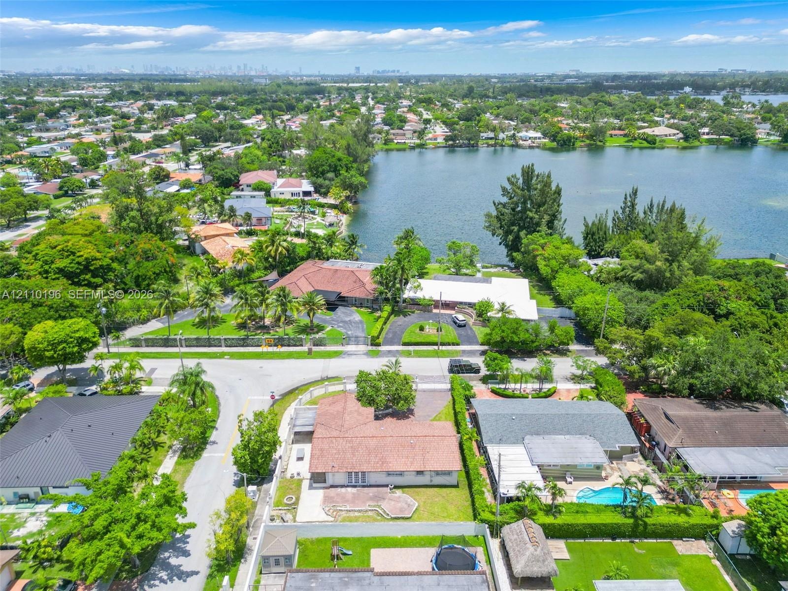 Aerial perspective of a multi-structure property featuring a sprawling tile roof, circular paved driveway, expansive waterfront acreage, and mature la