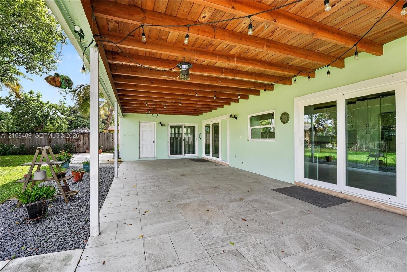 Covered patio featuring a wood-beam ceiling, large-format tile flooring, double glass sliding doors, and a wood privacy fence