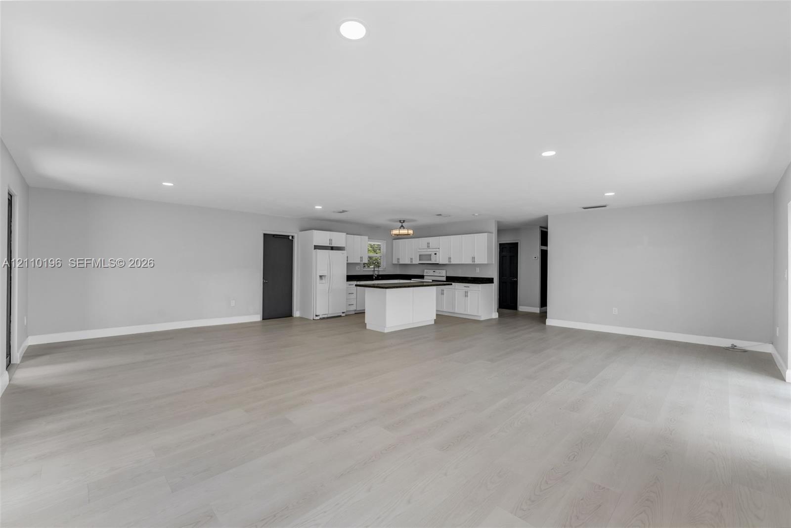 Open-concept interior featuring light wood-finish flooring, recessed lighting, and a kitchen equipped with white cabinetry, a center island, and dark-