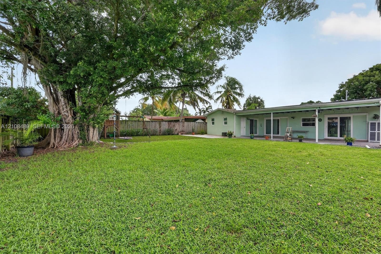 Expansive backyard featuring a large mature tree, a covered patio, and wood-paneled privacy fencing