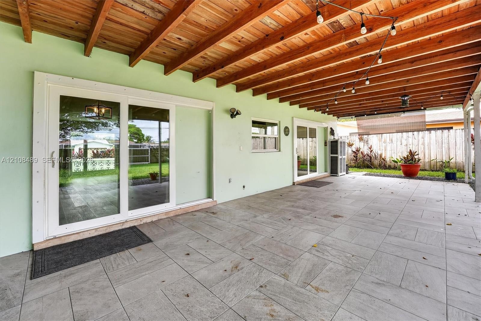 Covered patio featuring large-format stone-style tile flooring, exposed wood beam ceiling, dual sliding glass doors, and attached overhead string ligh