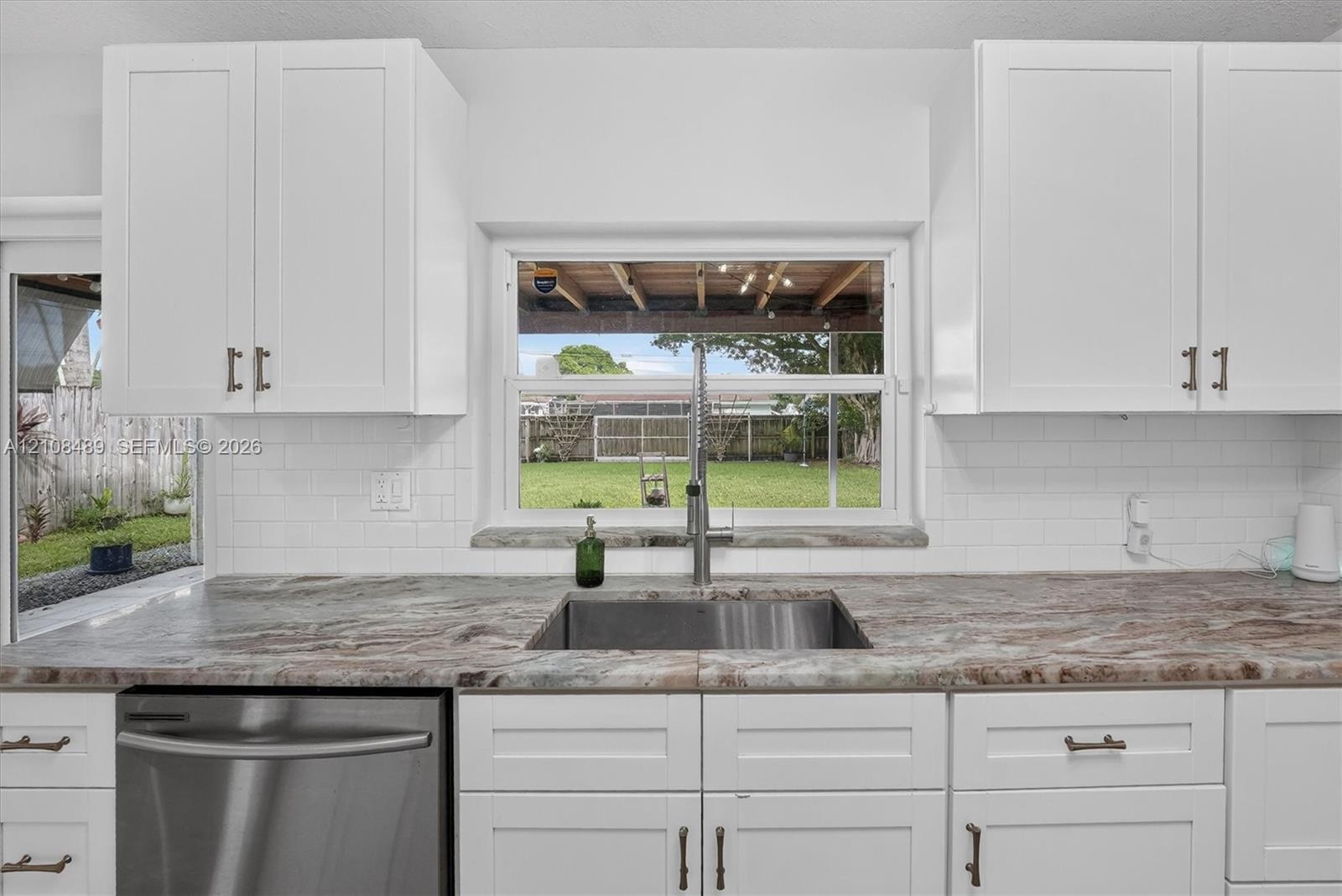 Kitchen featuring white shaker-style cabinetry, stone-patterned countertops, a stainless steel undermount sink with a gooseneck faucet, white subway t