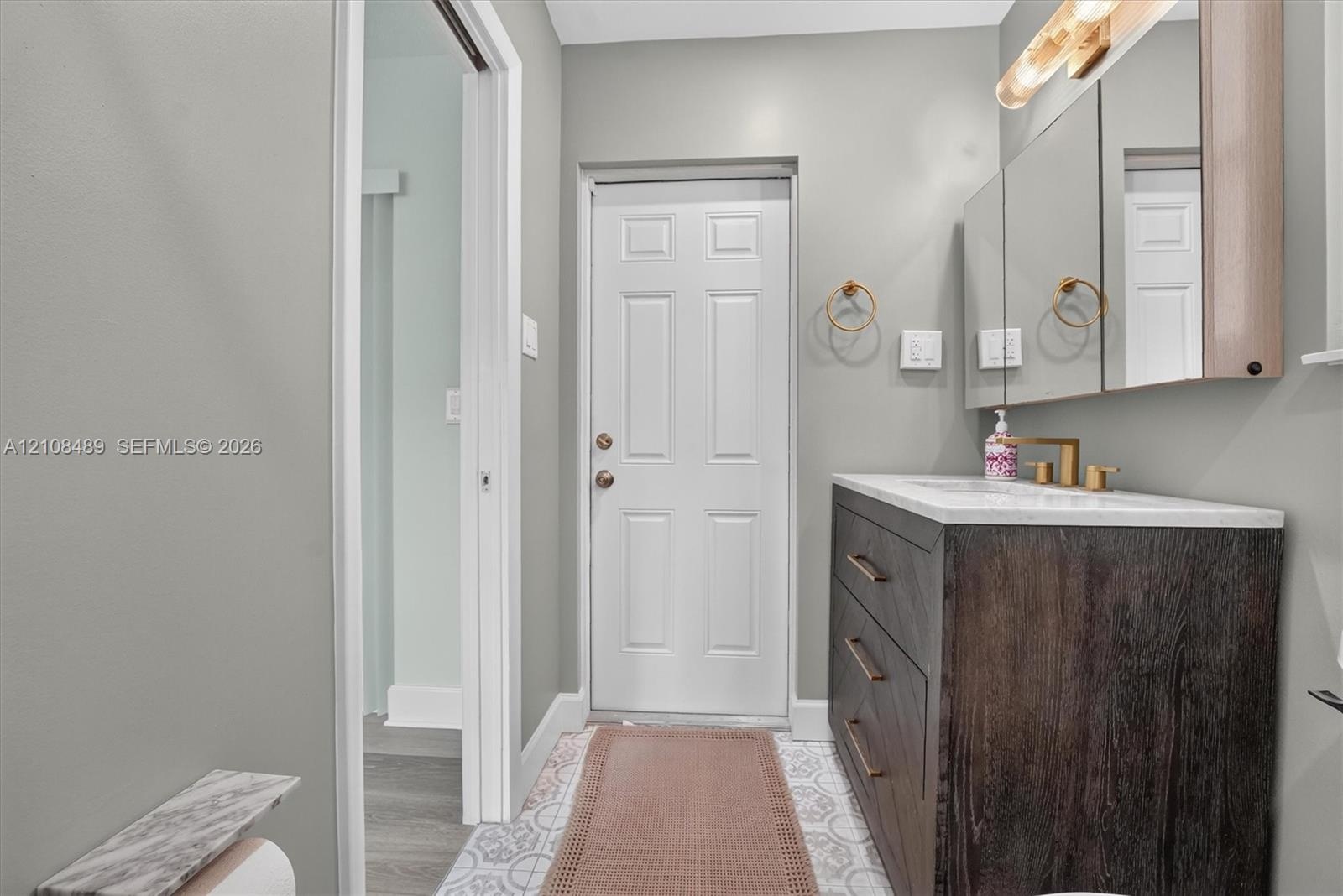 Bathroom vanity with dark wood-finish cabinetry, a stone-surface countertop, and gold-tone fixtures, complemented by decorative patterned floor tile a